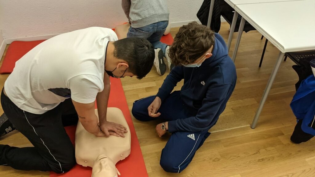 A student practises chest compressions on a CPR manikin while a classmate watches during an indoor class