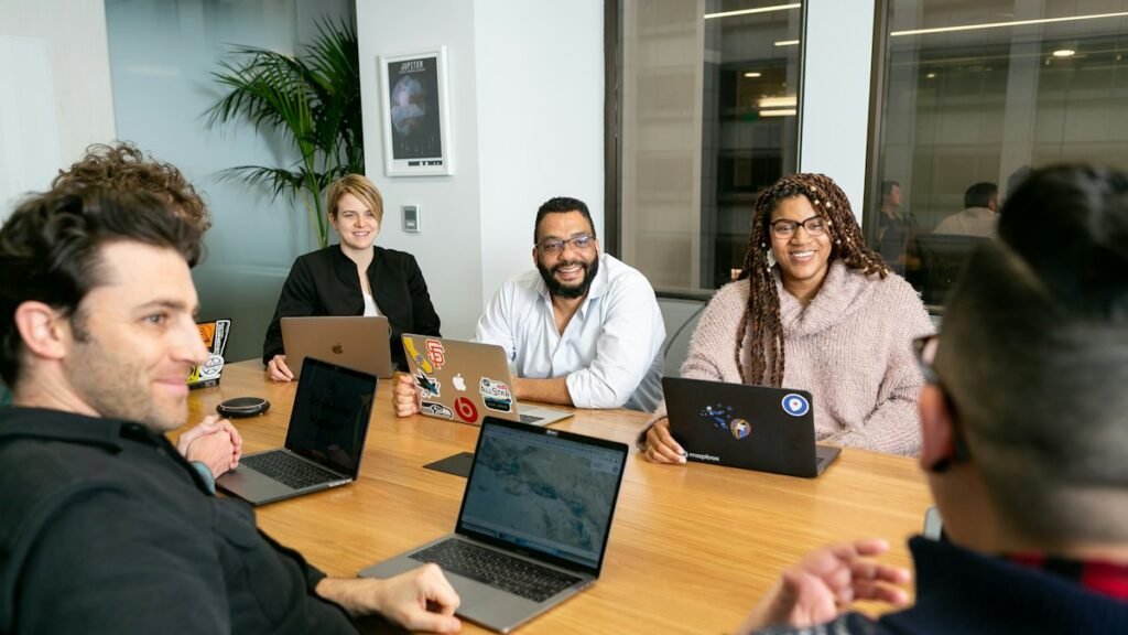 A team with laptops sits around a conference table, listening to a colleague during a meeting